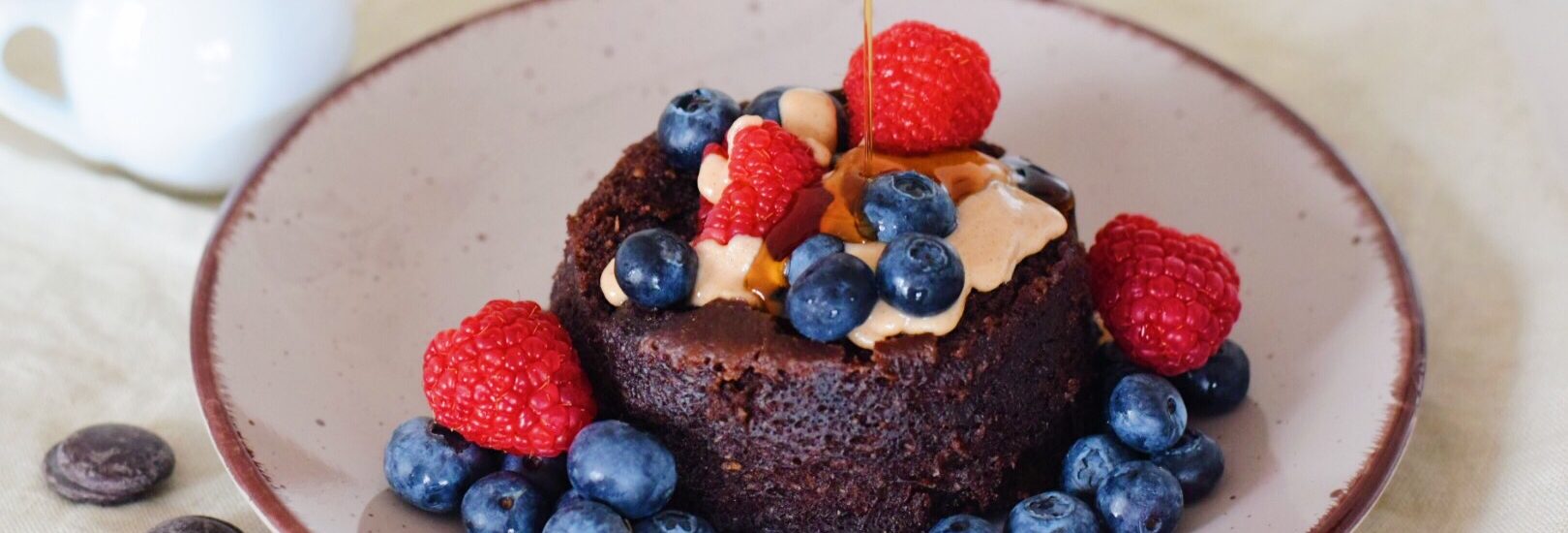 Zdravý čokoládový mug cake s ovocem, arašídovým máslem a politý javorovým sirupem. Veganský.